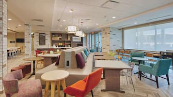 A modern lounge area with seating arrangements, a bar area, and a large window providing natural light.