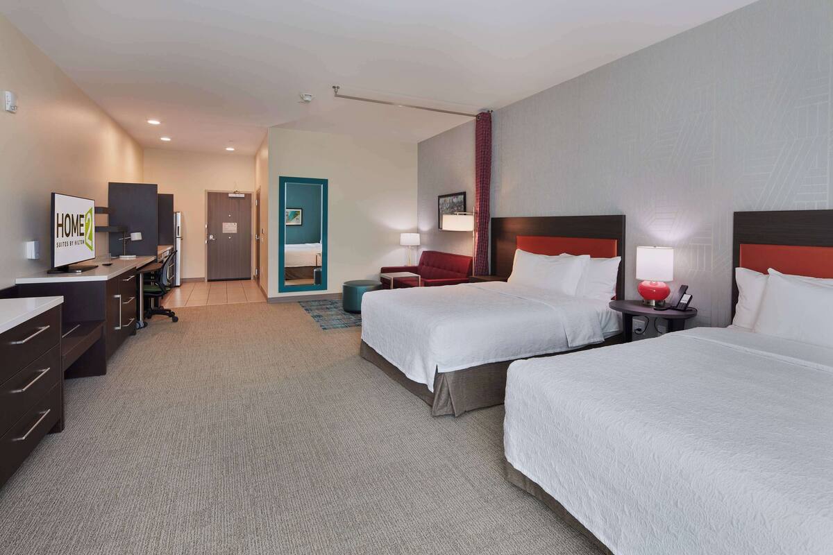 Een hotelkamer met twee bedden, een bureau met een computer, een televisie en een badkamers deur.