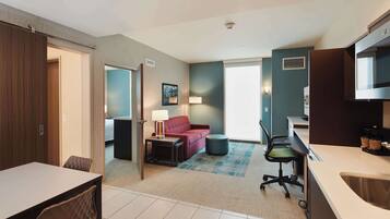 Hotelkamer met een eethoek, een zithoek met een bank en een lamp, een kitchenette en een groot raam.