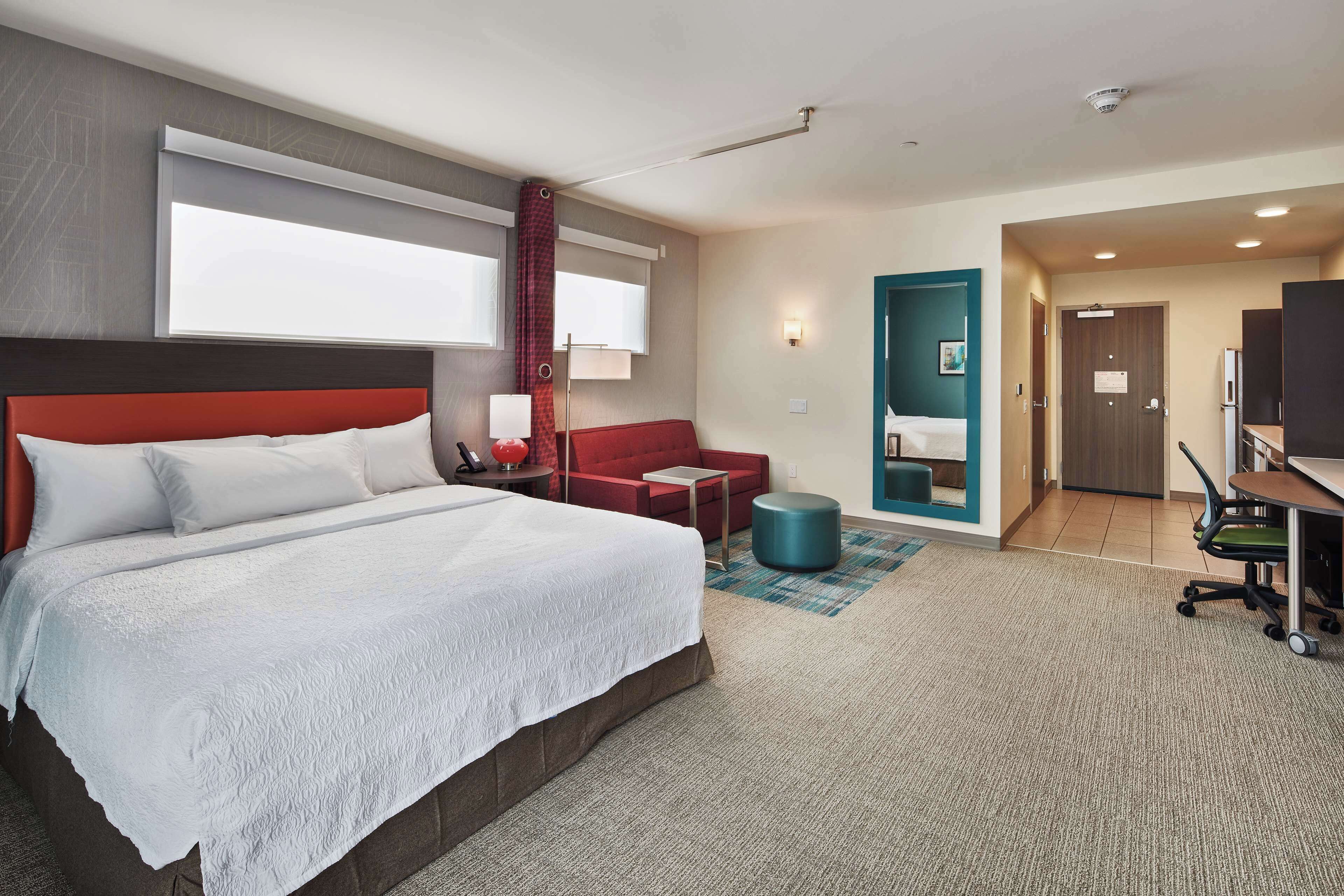 Una habitación de hotel con una cama grande, un escritorio, una silla, un sofá rojo y una televisión.