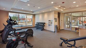 A gym with exercise equipment, a wall-mounted dumbbell rack, and a window with a view of the outside.