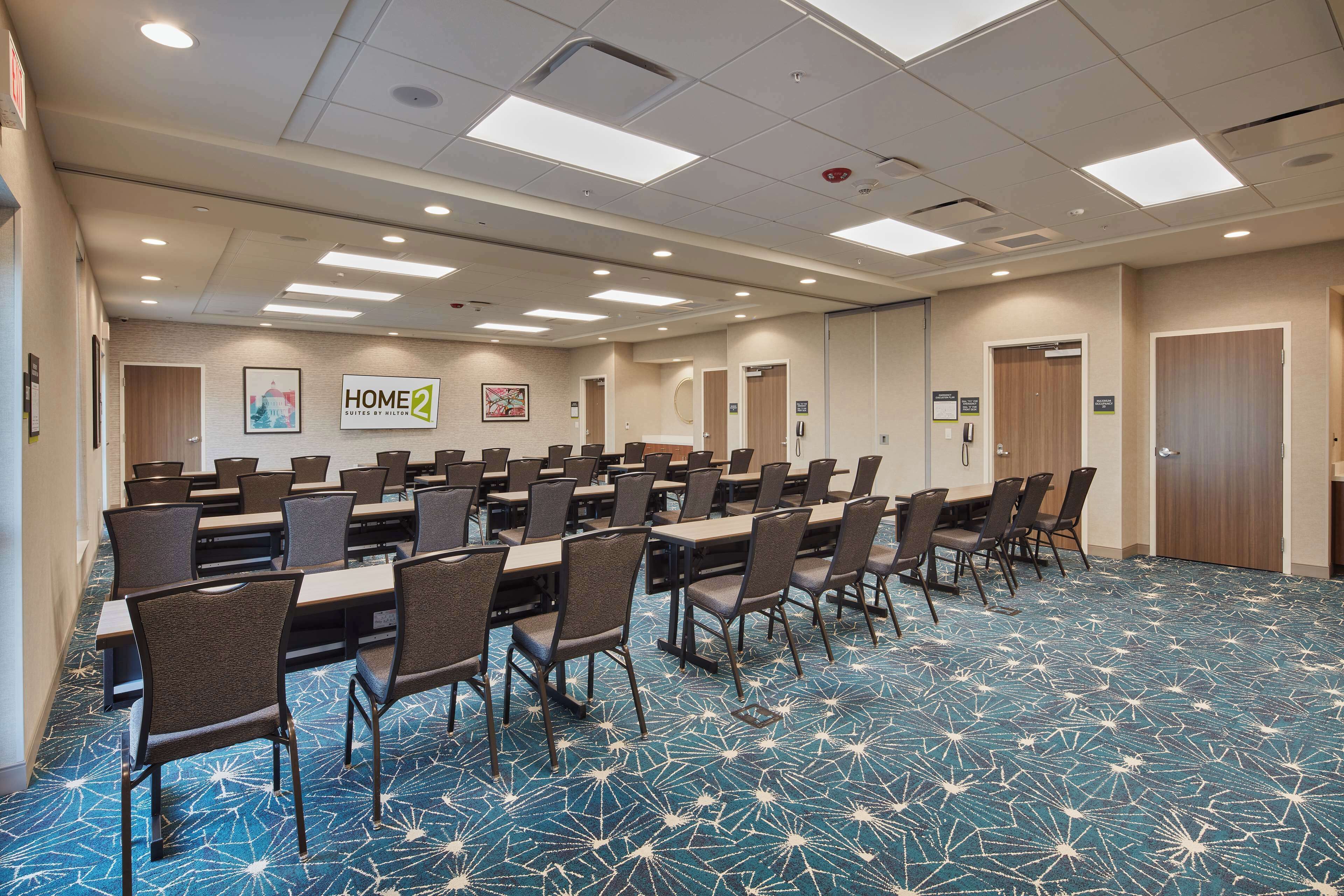 A large conference room with multiple tables and chairs, a patterned carpet, and several doors.