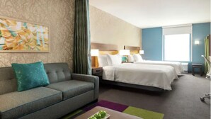 A hotel room with a sofa, two beds, a small table with apples, and a painting on the wall.