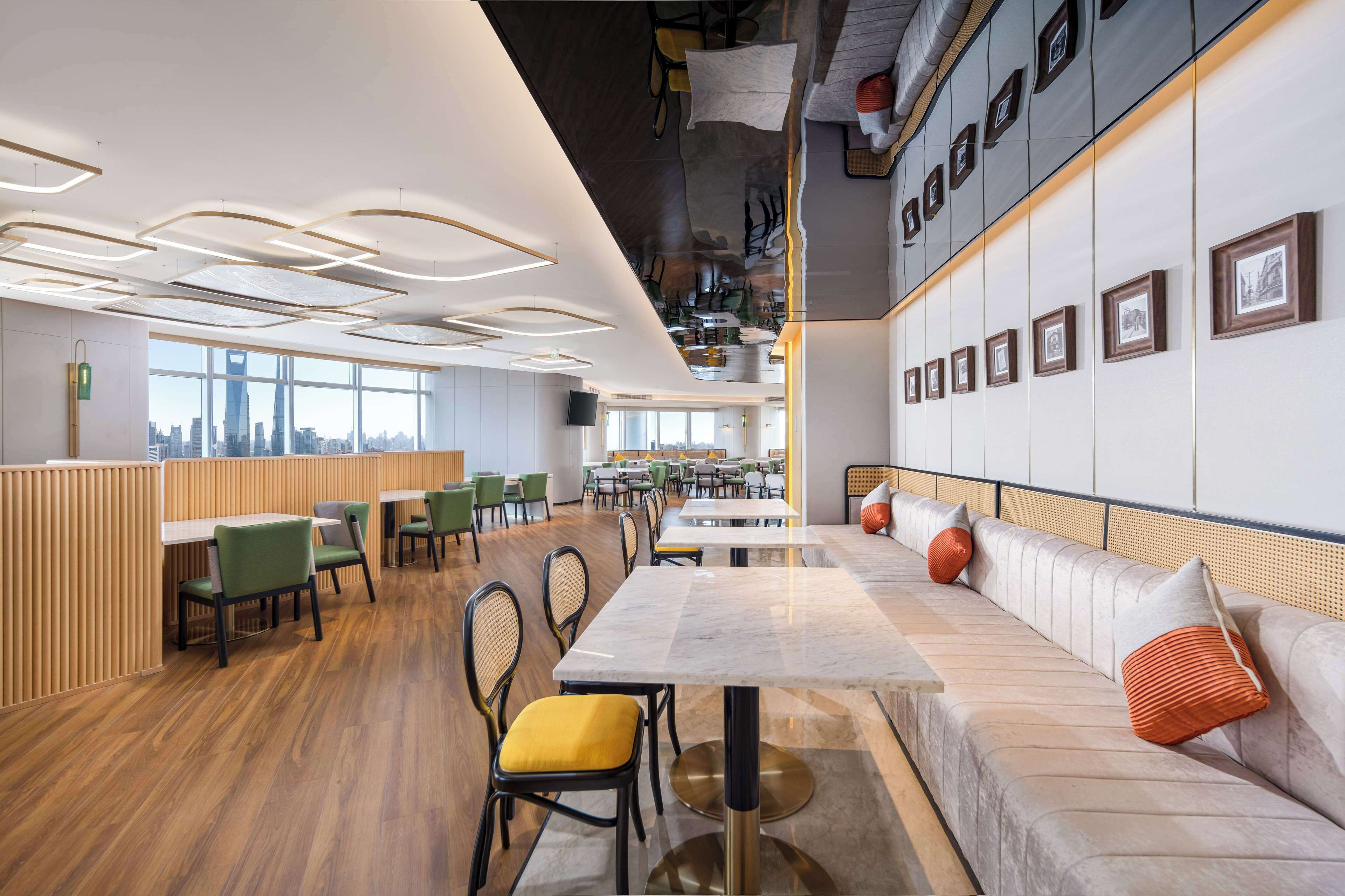 A modern restaurant with wooden flooring, green and yellow chairs, a marble table, and a sofa with orange cushions.