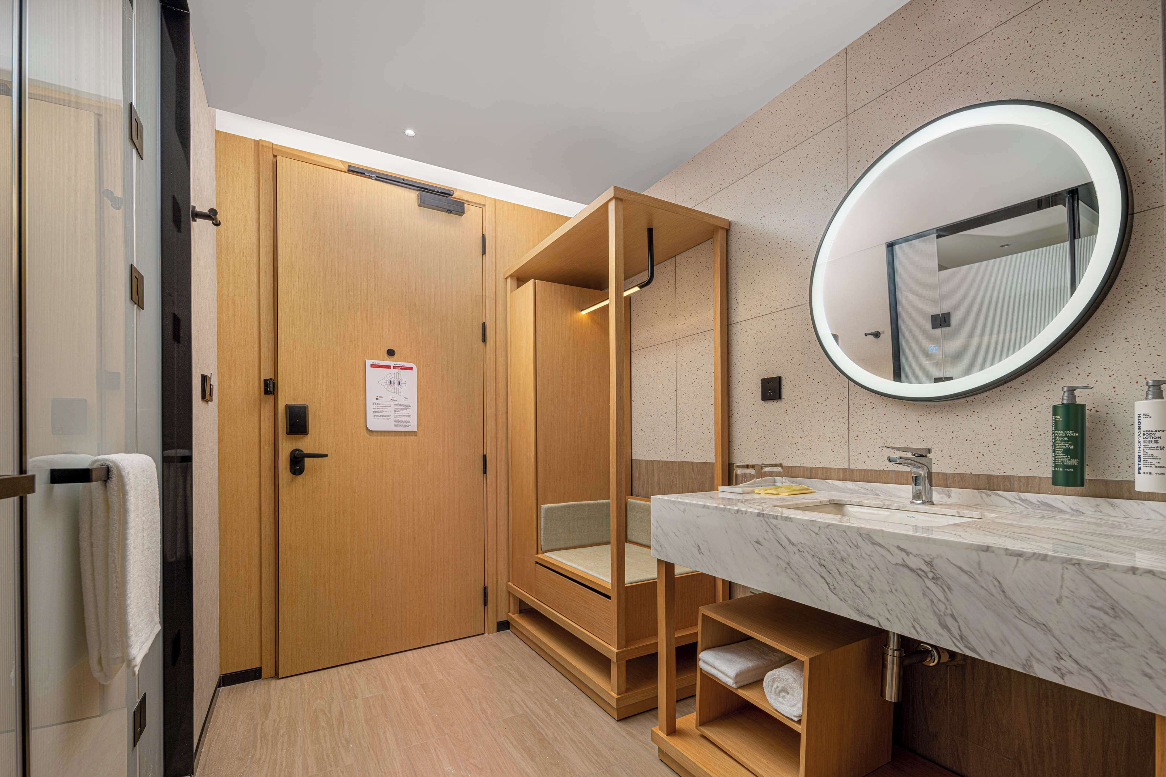 Un baño moderno con puerta de madera, lavamanos de mármol, un espejo y un perchero para toallas.