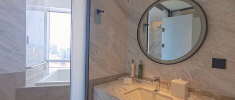 A modern bathroom with a marble sink, a round mirror, and a view of the city through a large window.
