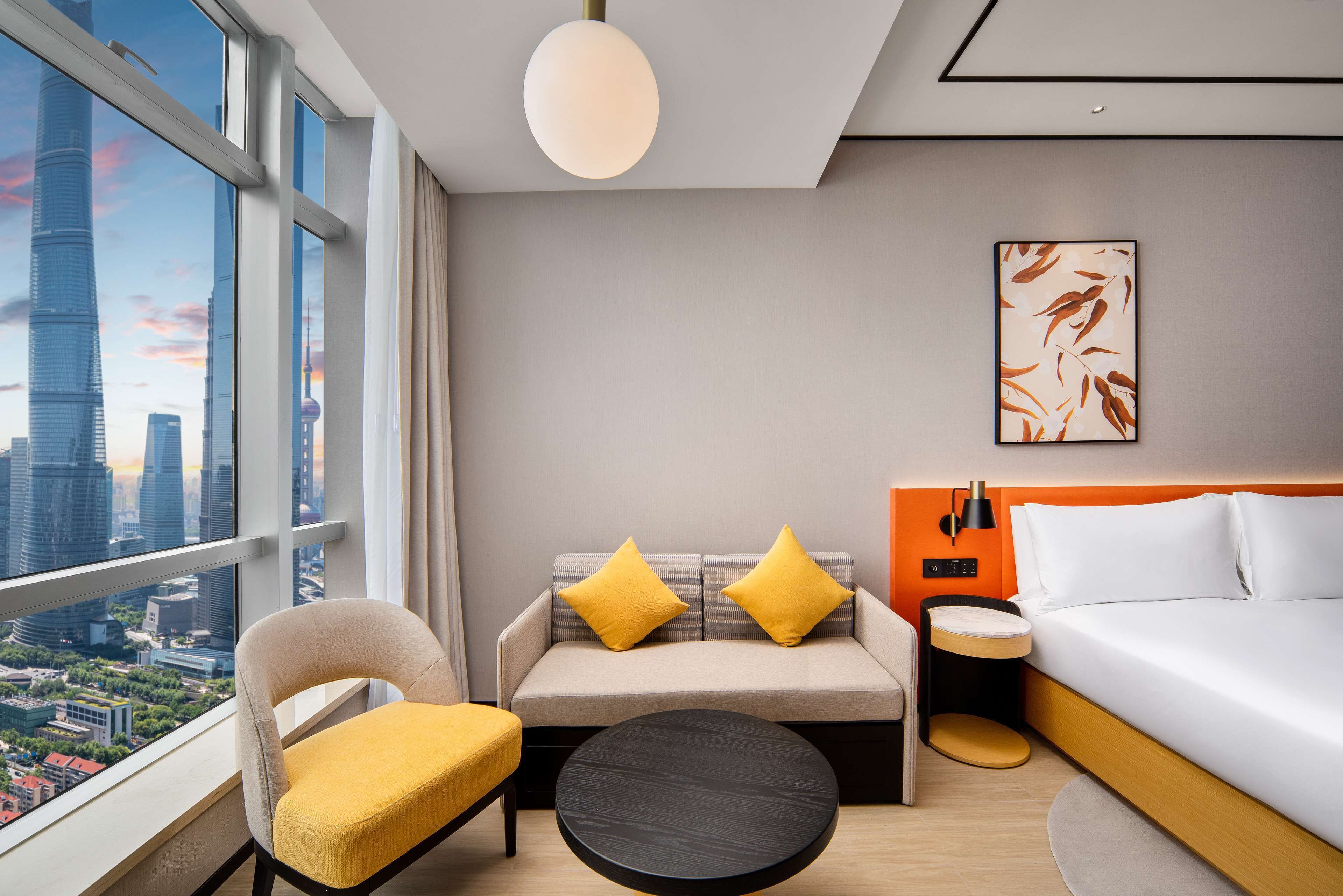 Ein modernes Hotelzimmer mit einer Couch, einem Bett, einem runden Tisch und Blick auf die Stadt.