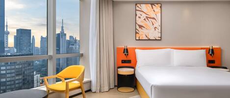 A hotel room with a large window, a bed, a chair, a table, and a city view.