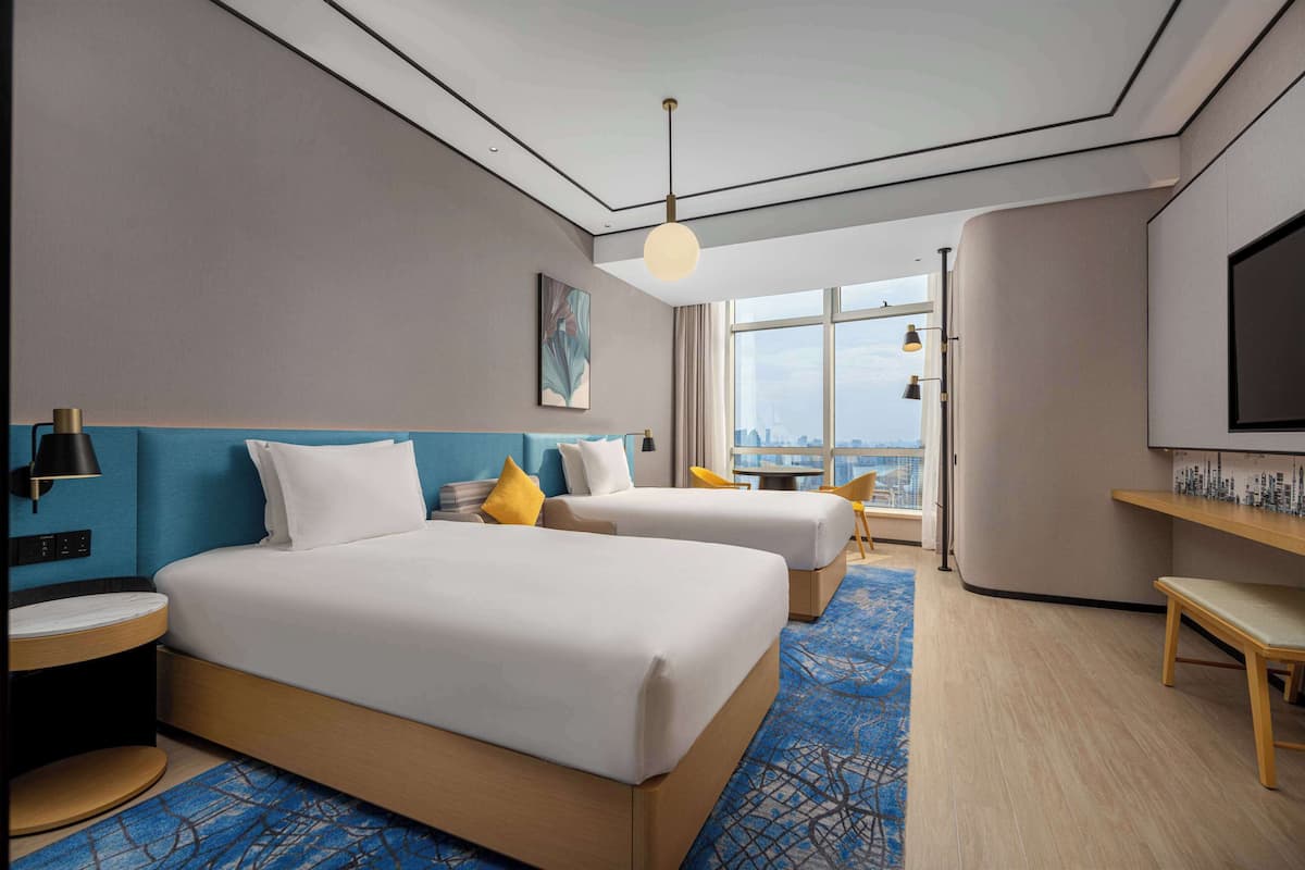 A hotel room with two beds, a city view, a TV, and a desk.