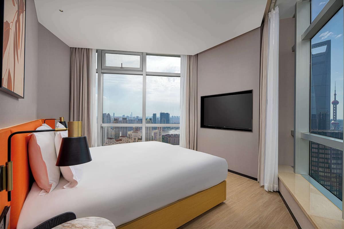 A modern hotel room with a large bed, a flat-screen TV, and a city view.