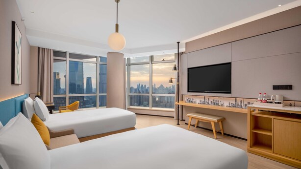 Une chambre d’hôtel moderne avec deux lits, une grande fenêtre donnant sur la ville, un téléviseur à écran plat et un petit bureau.
