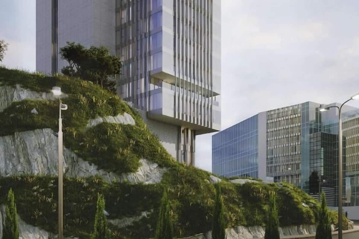 Een modern hoog gebouw met een opvallende glazen gevel, gelegen in een aangelegd gebied met een rotsformatie en groen.