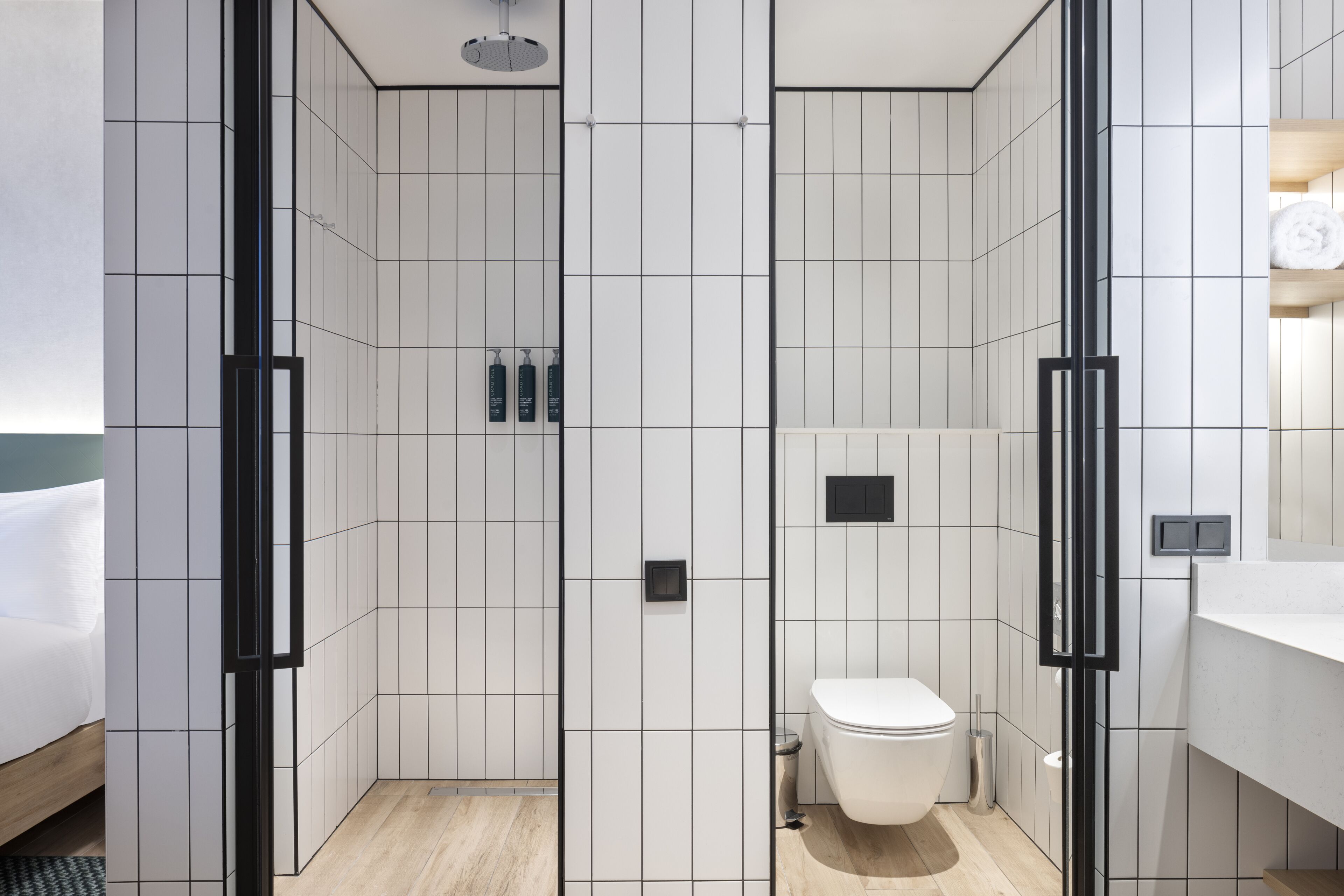 Une salle de bain moderne avec des murs recouverts de carreaux blancs, des toilettes et un espace douche.