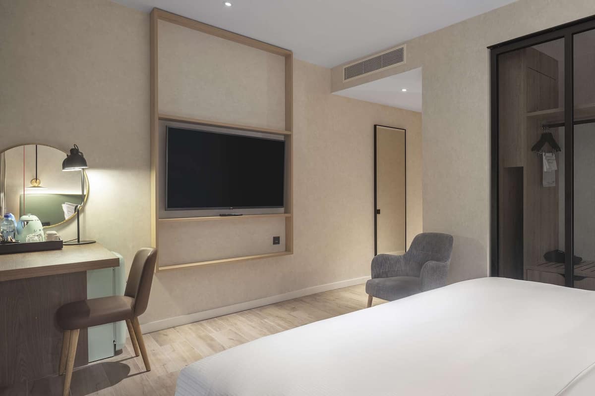 Een hotelkamer met een bed, een bureau met een computer, een stoel, een televisie en een groot raam.
