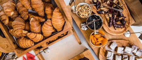 A variety of pastries and desserts on wooden trays, including croissants, muffins, and a cake with powdered sugar.
