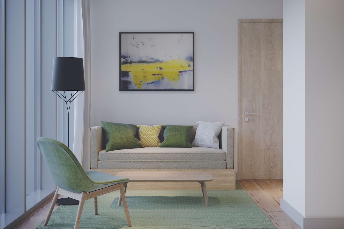 Een moderne woonkamer met een grijze bank, groene en gele kussens, een groene fauteuil en een vloerlamp.