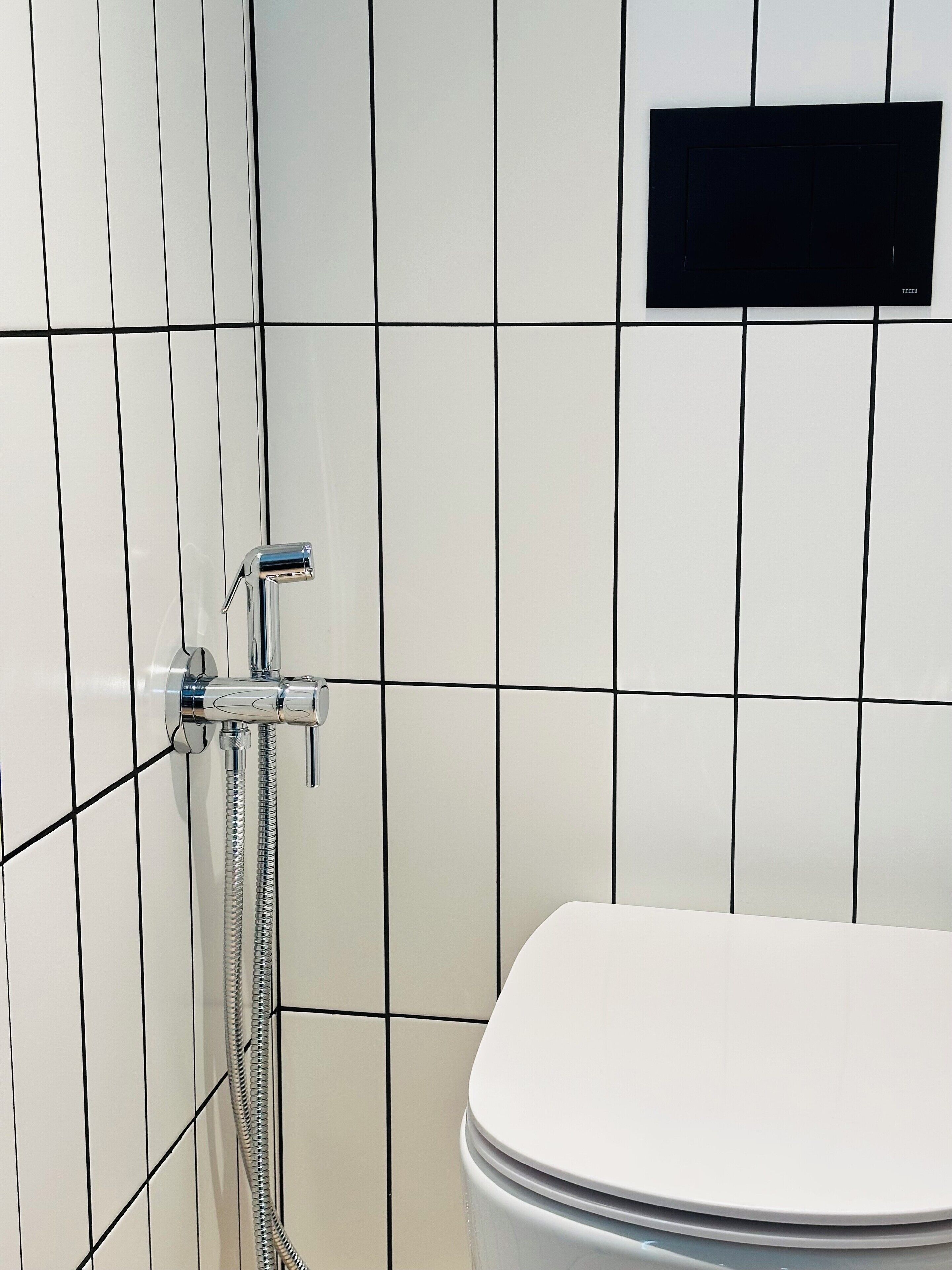 A bathroom with white tiled walls, a chrome showerhead, and a white toilet.