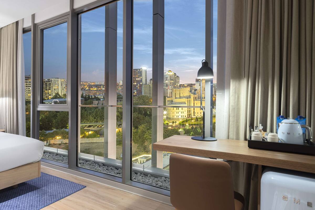 Een moderne hotelkamer met een groot bed, een bureau en uitzicht op de stad.