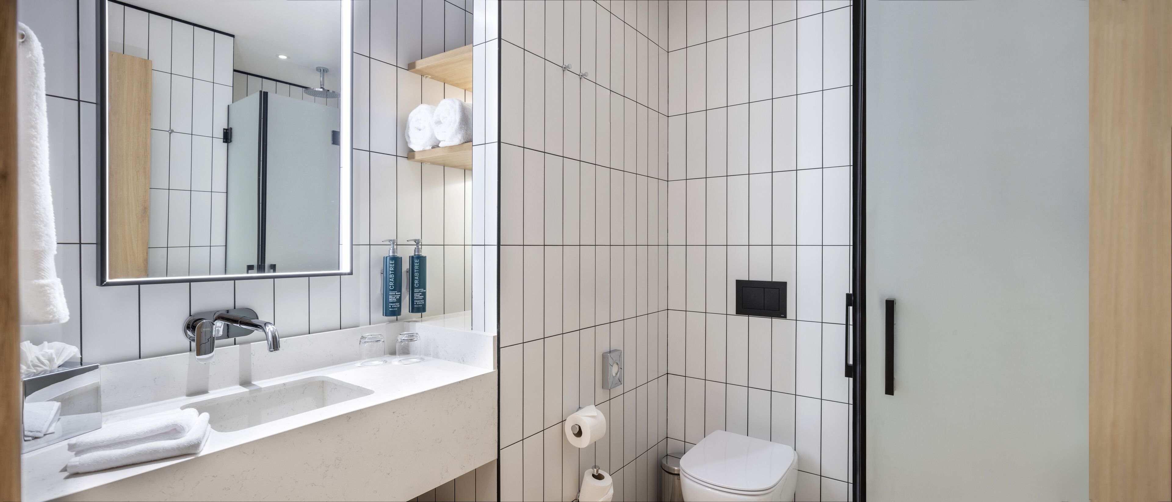 A modern bathroom with a large mirror, white sink, and a toilet.