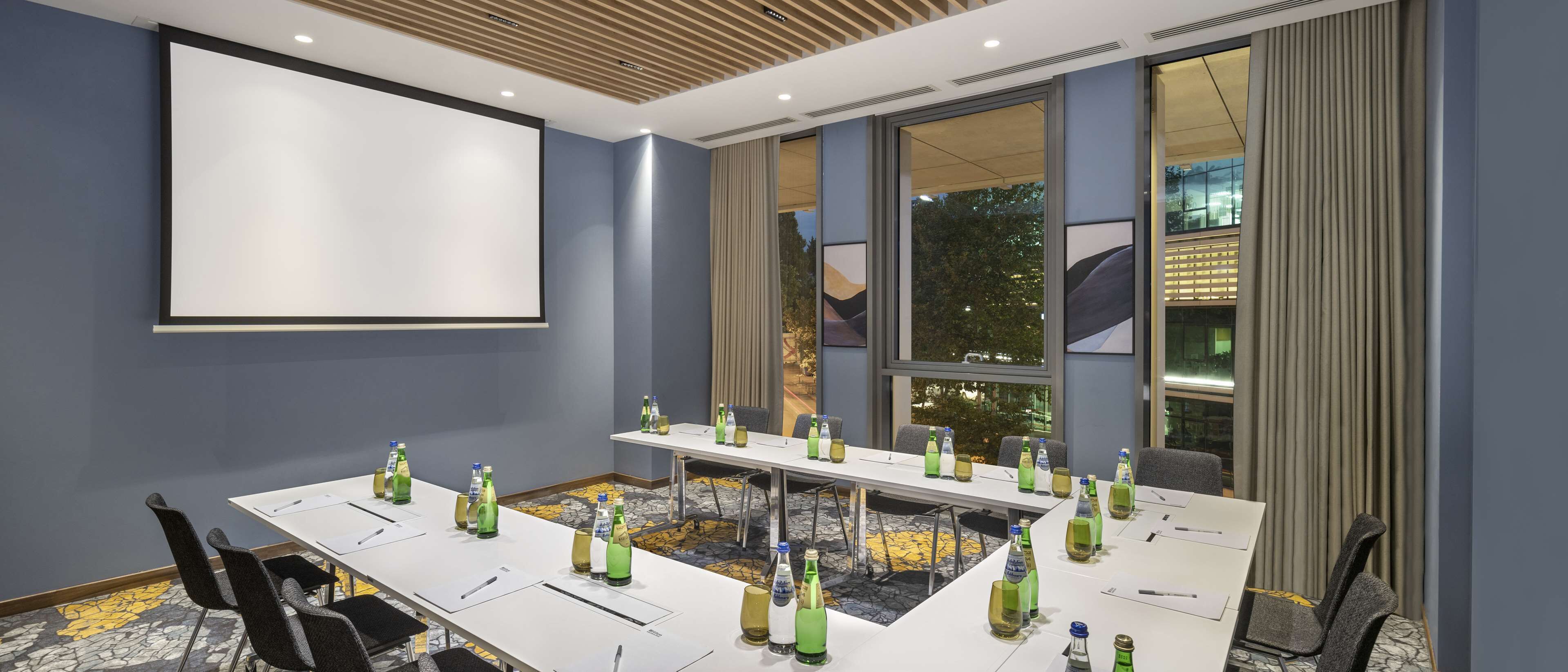 A conference room with a long table, chairs, and a projector screen.