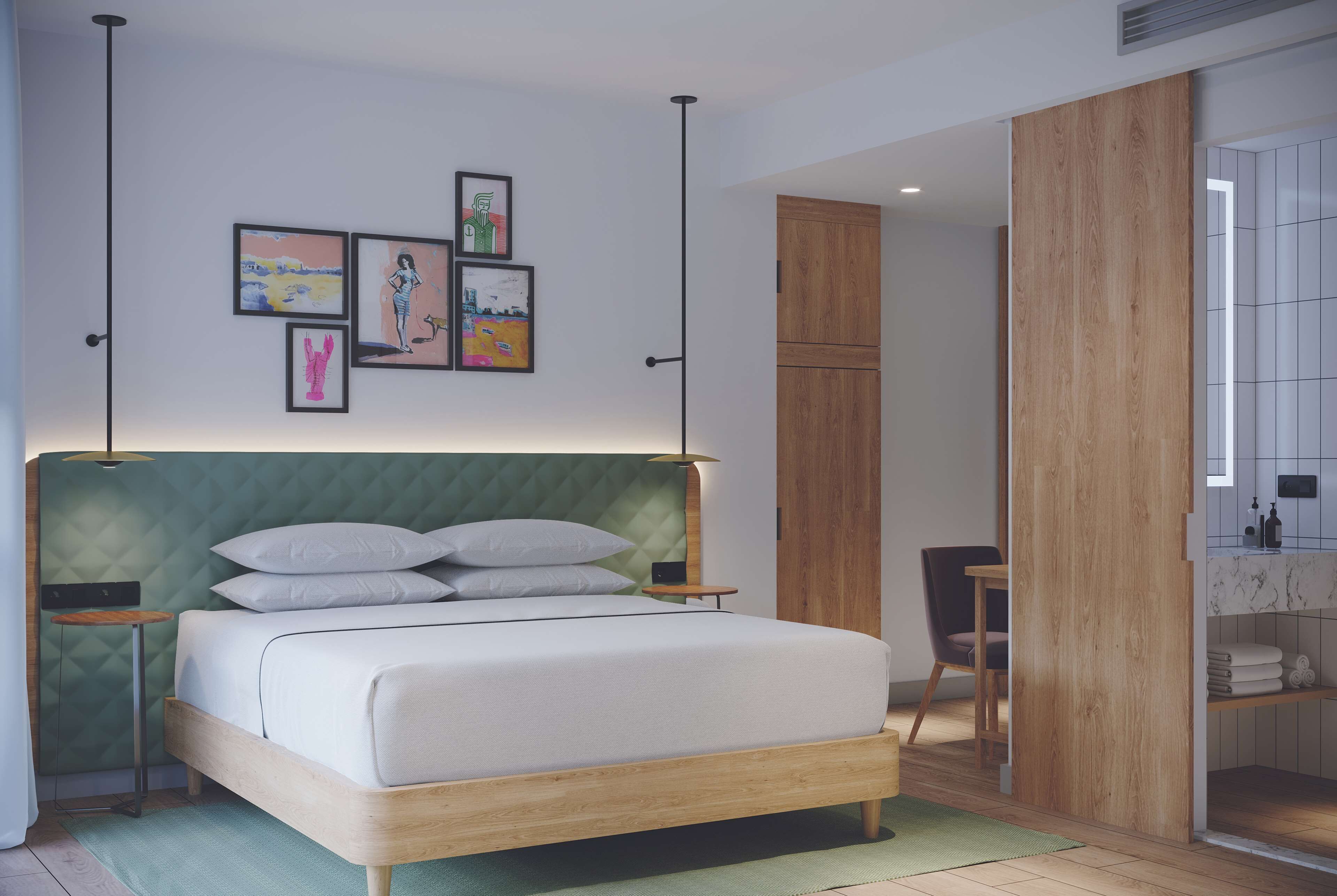 A modern bedroom with a green upholstered headboard, a wooden bed frame, and a bedside table with a lamp. There are framed pictures on the wall, a wooden wardrobe, and a bathroom visible through an open door.