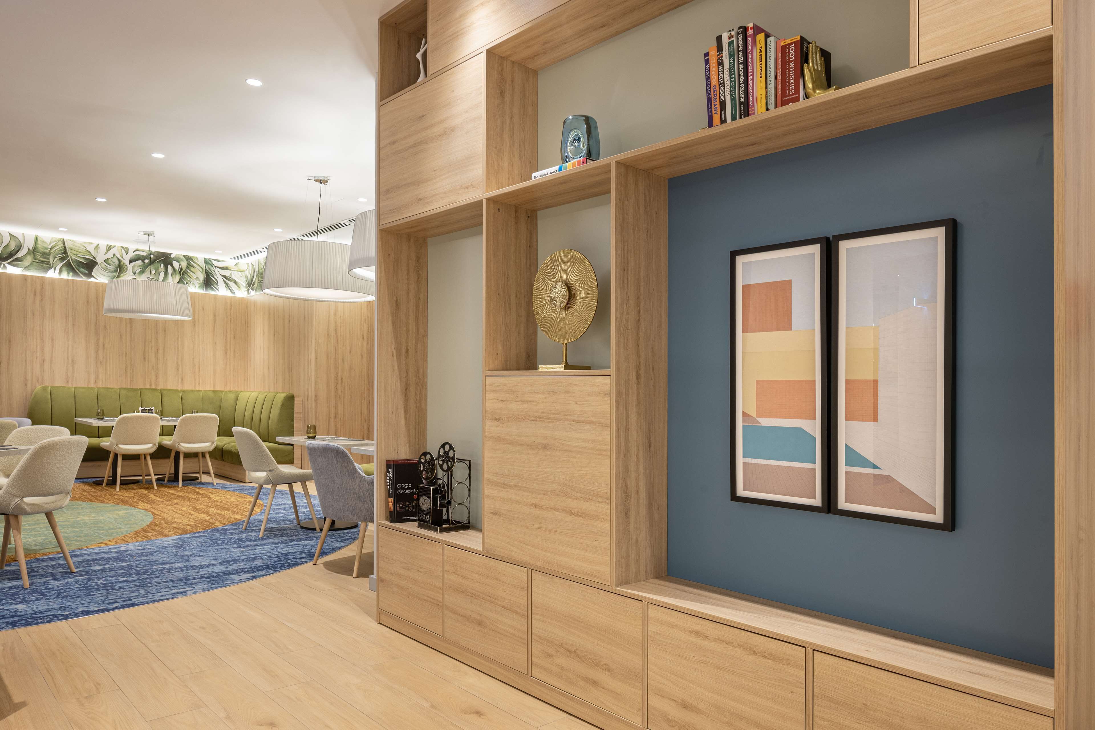 A modern interior with a green sofa, white chairs, a blue rug, and wooden shelves with books and decorative items.
