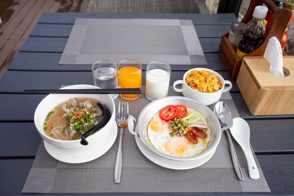 A table set with a bowl of soup, a plate of eggs, a bowl of cereal, and glasses of orange juice and milk. - Chewa Khong Nakhon Phanom (Nakhon Phanom)