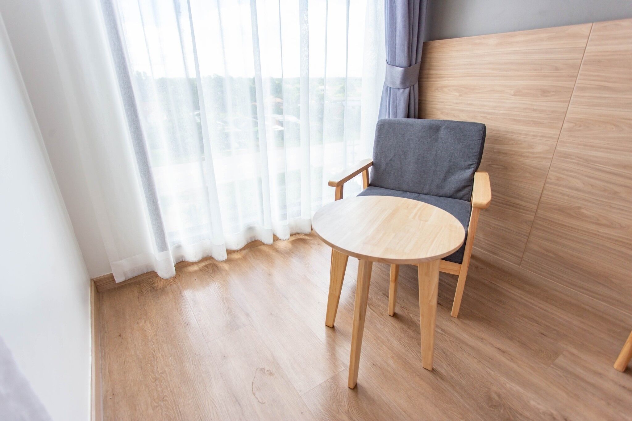 Quarto com piso de madeira, uma cadeira cinza e uma mesa redonda de madeira.