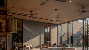 Ein großzügiges, modernes Interieur mit hohen Decken, Deckenventilatoren und großen Fenstern mit Blick ins Freie.