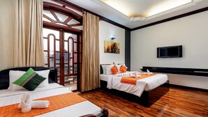 A hotel room with two beds, wooden flooring, a TV, and a painting on the wall.