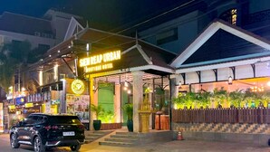 A hotel entrance with a neon sign, a car parked in front, and a gated area with plants.