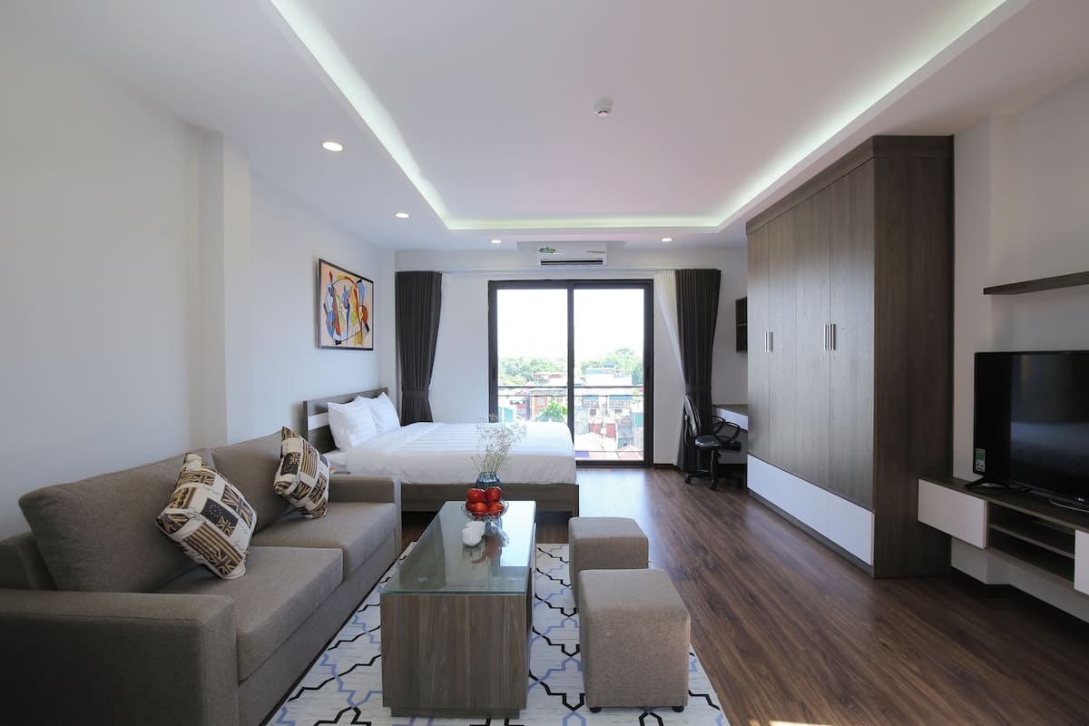 A modern hotel room with a bed, sofa, TV, and a balcony with a view.