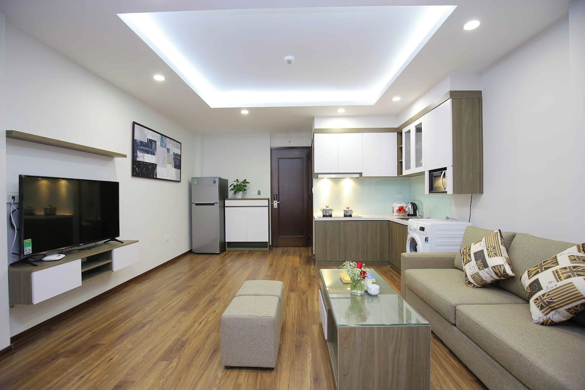 A modern living room with a flat-screen TV, a glass coffee table, and a sofa with patterned cushions.