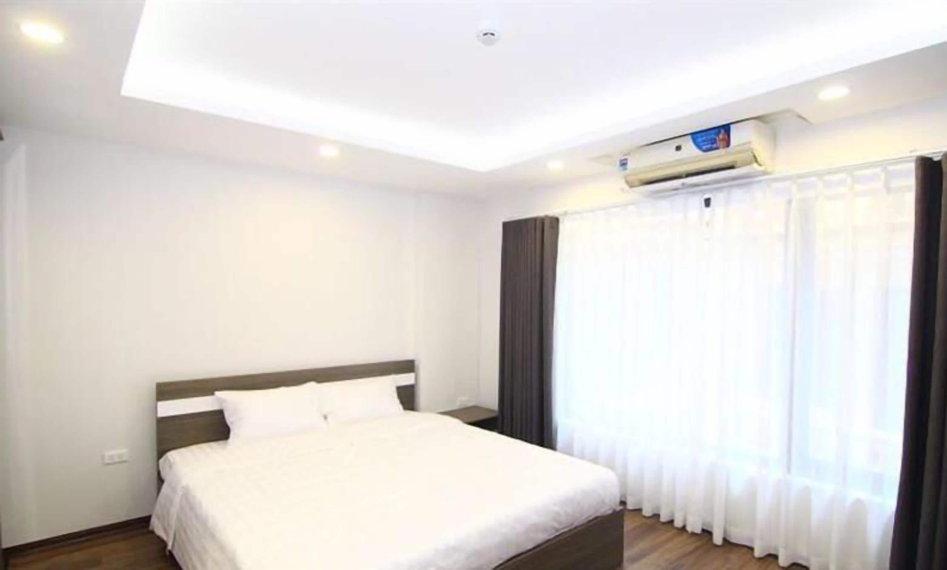 Quarto de hotel com cama, mesa de cabeceira, janela com cortinas e aparelho de ar condicionado na parede.