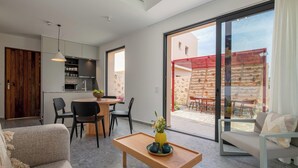 Un espace de vie moderne comprenant un canapé, une table en bois, un coin cuisine et une porte-fenêtre coulissante donnant sur une terrasse extérieure.