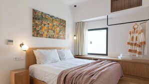 Une chambre d’hôtel moderne avec un grand lit, une table de chevet, une œuvre d’art accrochée au mur, une fenêtre avec des rideaux et un porte-serviettes avec des serviettes.
