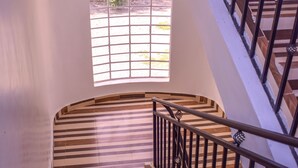 A spiral staircase with wooden steps and metal railings, leading to a window with a view of greenery outside. - Rio Breeze Gardens (Nairobi)