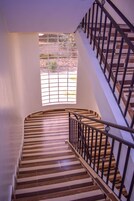 A spiral staircase with wooden steps and metal railings, leading to a window with a view of greenery outside.
