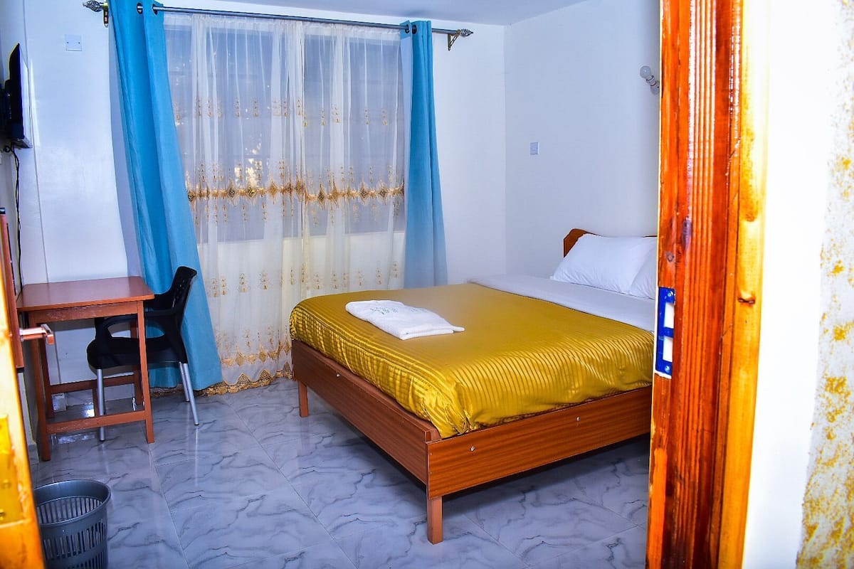A bedroom with a wooden bed, a desk, a chair, and a window with blue curtains.