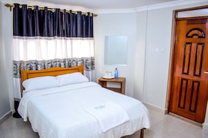 Una cama bien hecha con ropa blanca, cabecera de madera y mesita de noche con una botella y vasos.