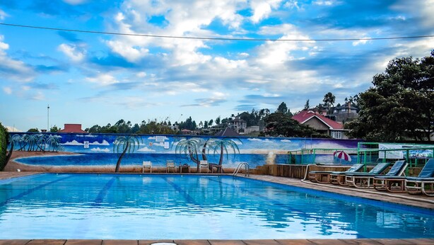 A swimming pool with lounge chairs and a mural of palm trees. - Rio Breeze Gardens (Nairobi)