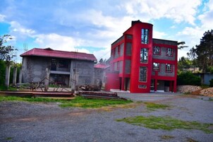 A two-story building with a red facade and a red roof, surrounded by a gravel driveway and greenery.