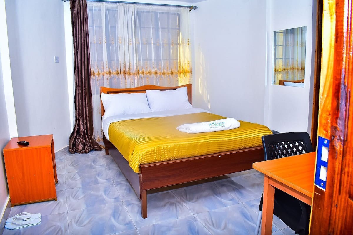 A hotel room with a bed, a wooden nightstand, a desk, and a chair.