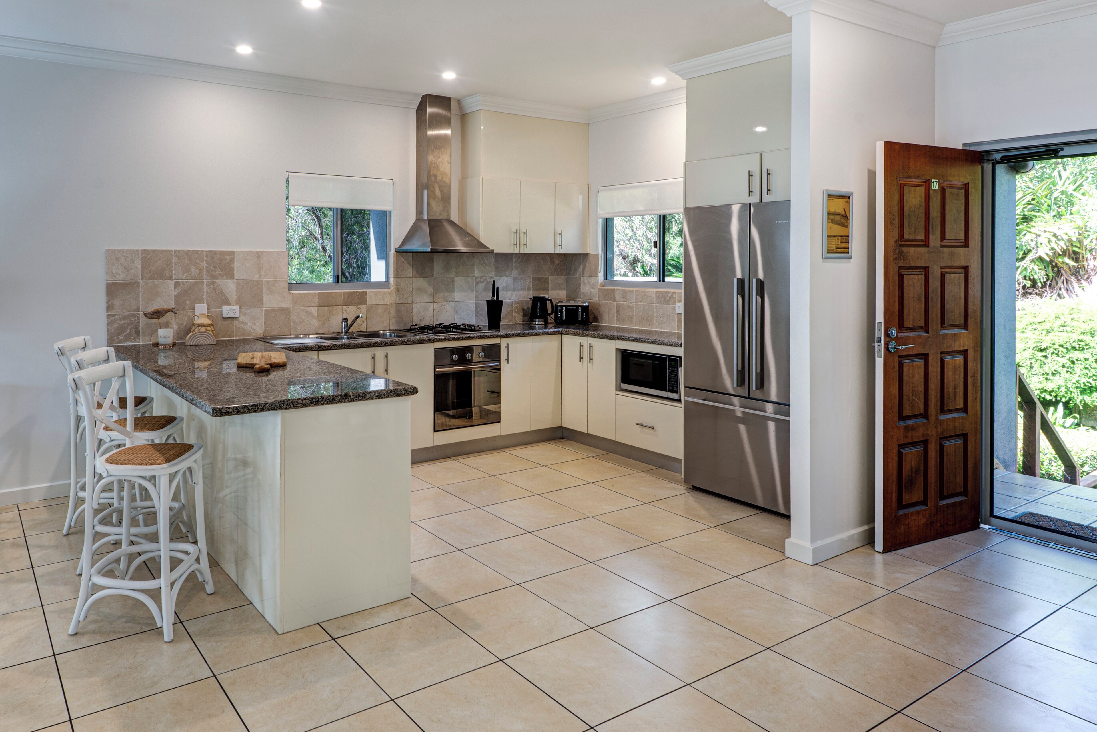 A modern kitchen with white cabinets, a stainless steel refrigerator, and a large island with bar stools.
