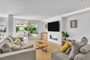Een moderne woonkamer met een bank, salontafel en televisie. Er is een schuifdeur die leidt naar een terras.