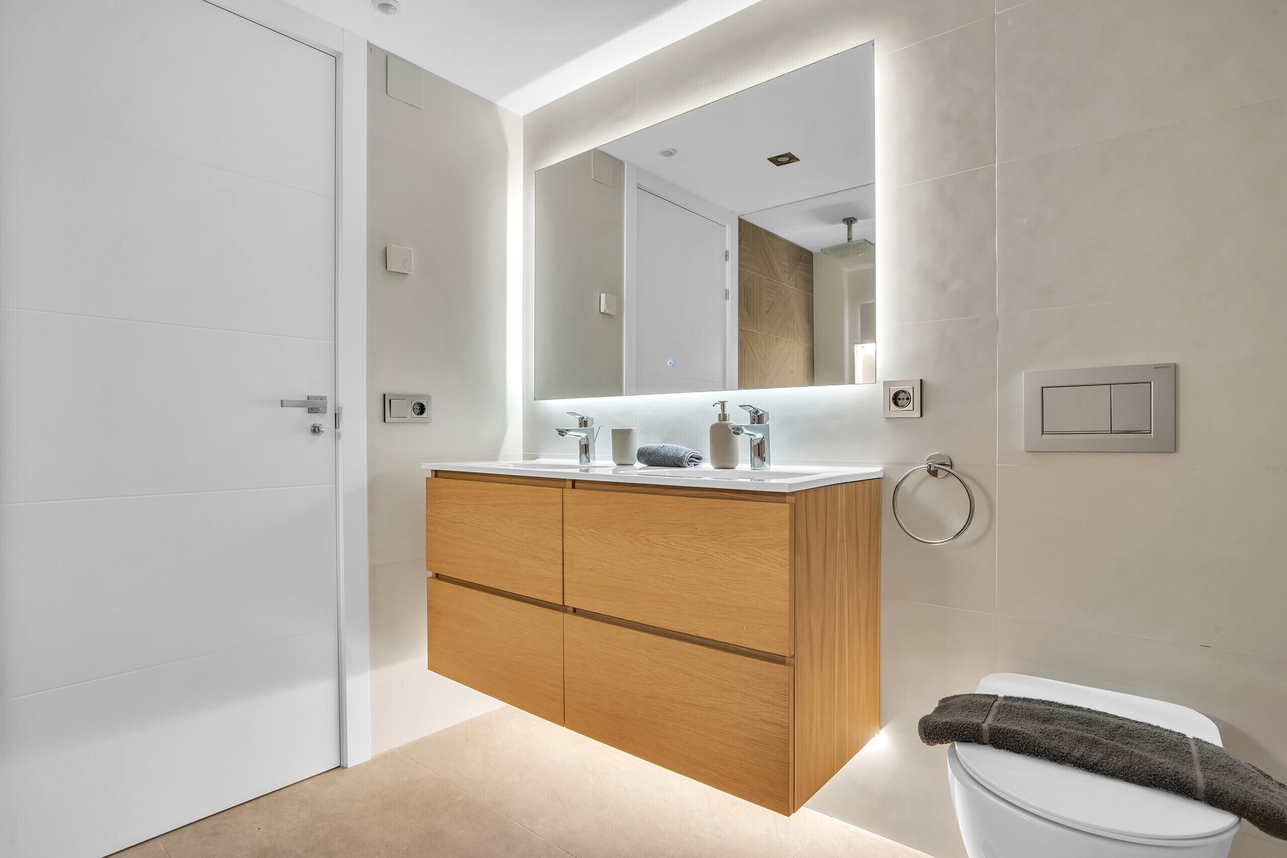 Un baño moderno con tocador de madera, un espejo grande y un inodoro.