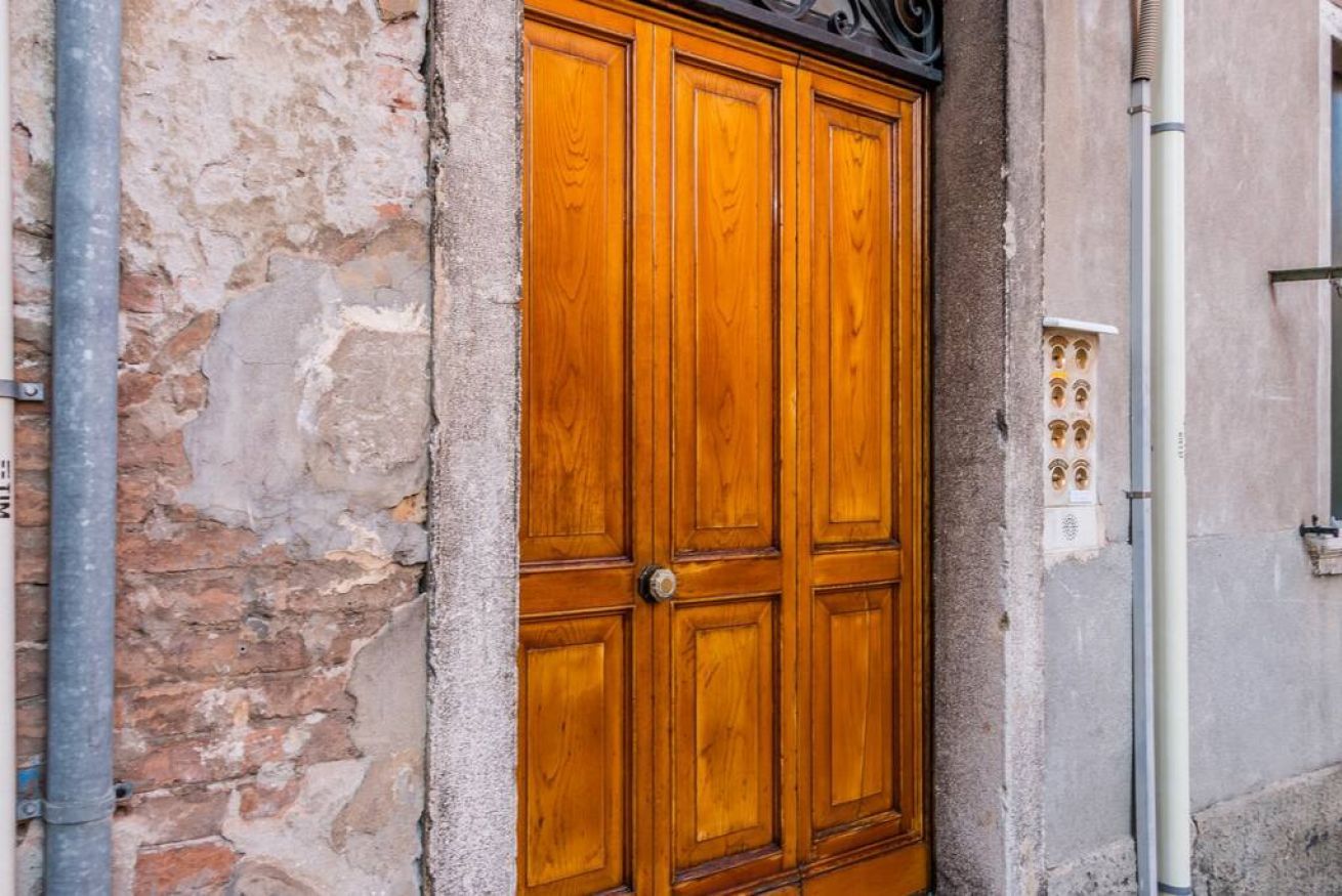 Una puerta doble de madera con un picaporte de metal, empotrada en un muro de piedra con una caja de servicios cercana.