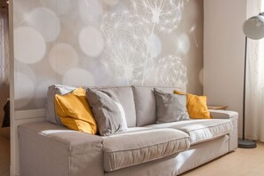 Ein modernes Wohnzimmer mit einer Couch, Kissen, einer Stehlampe und einer Wand mit einem Löwenzahn-Muster.