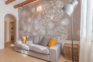 A living room with a grey sofa, yellow cushions, a floor lamp, and a wall with a dandelion pattern.