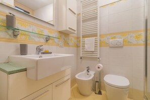 A bathroom with a sink, bidet, toilet, and a glass shelf above the sink. - Casa Masa close to @S. Lucia Train Station (Venezia)